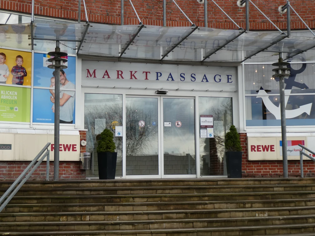 Eingang Markpassage Eingang zur Markpassage mit Glastüren, flankiert von zwei Pflanzkübeln auf einer steinernen Treppe.
