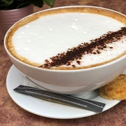 Eine große Tasse Milchkaffee, gekrönt mit Schaum und Kakaopulver, auf Untertasse mit Gebäck.