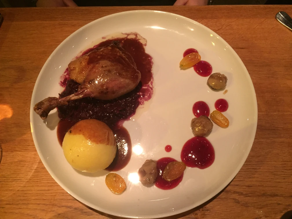 Gans Ein Teller mit Entenkeule auf Rotkohl, begleitet von Knödeln, Trauben und ansprechender Sauce.