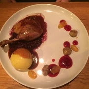 Gans Ein Teller mit Entenkeule auf Rotkohl, begleitet von Knödeln, Trauben und ansprechender Sauce.