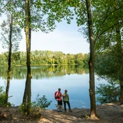 Blick auf den Menzelsee bei Hilden Zwei Personen stehen am Waldufer und blicken auf den ruhigen Menzelsee mit grüner Vegetation.