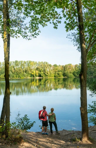 Blick auf den Menzelsee bei Hilden Zwei Personen stehen am Waldufer und blicken auf den ruhigen Menzelsee mit grüner Vegetation.