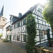 Ausflug zum historischen Stadtkern von Hilden Fachwerkhaus an gepflasterter Straße mit Kirchturm im Hintergrund. Sonniger Tag in Hilden.