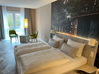 Thöles Hotel in Vilsen Zwei komfortable Einzelbetten in modernem Raum mit großem Fenster und Wandbild einer historischen Lokomotive.