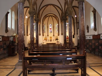 Romanische Kirche mit beeindruckenden Säulenreihen, bunten Glasfenstern und einem Altar im Hintergrund.