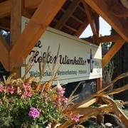 De Holter Wienkeller in Holte, Gemeinde Rhauderfehn, DSC01033.JPG Holzunterstand mit Schild für Weingut Ulienkeller, davor Blumenkasten mit pinken Blüten und getrockneten Gräsern.