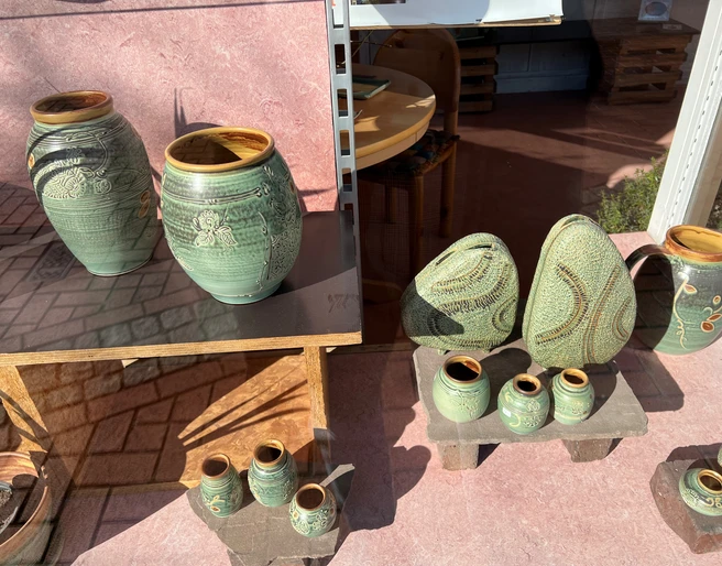 Keramikwerkstatt Luchtmann Verschiedene handgefertigte Keramikvasen und Objekte mit grüner Glasur und floralen Verzierungen.