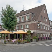 Ecke in einer deutschen Stadt mit Fachwerkhaus, Café mit gelben Schirmen und blühenden Pflanzen.