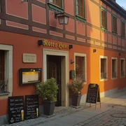 Fachwerkhaus mit roter Fassade und grünen Fensterläden, beschriftet als "Rotes Haus", mit Menütafeln und Pflanzen vor der Tür.