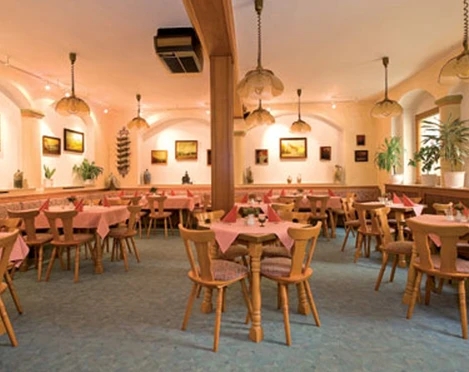 Gastraum Gemütliches Restaurant mit Holzmöbeln, runden Tischen und rosa Tischdecken, umgeben von Pflanzen und Bildern an den Wänden.