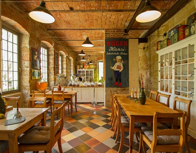 Adoratio Schokoladenkunst Gemütliches Café mit Holztischen und Stühlen, buntem Fliesenboden, Ziegelwänden und nostalgischem Poster; warme, einladende Atmosphäre.