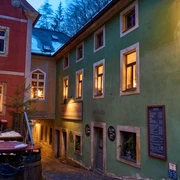 Bio-Bäckerei im Winter Enge Gasse mit einer rot-grünen Bäckerei, beleuchtet von warmem Licht, weihnachtliche Dekorationen in den Fenstern, winterliche Atmosphäre.