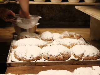 Traditioneller Stollen in der Bio-Bäckerei in Schmilka Bäcker bestäubt frisch gebackene Stollen mit Puderzucker; die Stollen liegen auf einem Backblech in einer rustikalen Bäckerei.