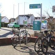 Ladestation auf dem Marktplatz Fahrräder parken bei einer E-Bike-Ladestation an einer Straße, im Hintergrund sind Häuser zu sehen.