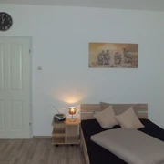 Ein schlicht eingerichtetes Schlafzimmer mit einem Bett, einem Nachttisch, einer Lampe und einer Wanduhr.