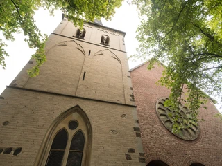 Kirche St. Gereon in Monheim am Rhein St.-Gereon-Kirche in Monheim am Rhein mit markantem Turm und gotischen Fenstern, von Bäumen umgeben.
