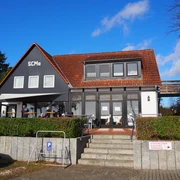 San Stefan  Ein zweigeschossiges graues Gebäude mit roten Dachziegeln und einer Terrasse unter blauem Himmel.
