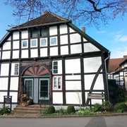 Fachwerkhaus mit markanter Architektur, bunte Tür, gepflegte Vorgartenanlage, blauer Himmel.