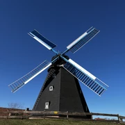 Windmühle Paula Windmühle Paula mit schwarzen Flügeln und tiefblauem Himmel im Hintergrund, umgeben von Holzzaun.