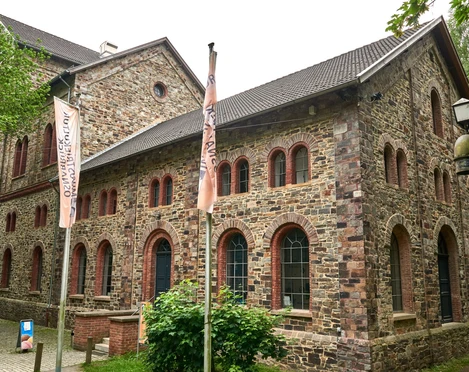museum_industriekulturfoto_achim_meurer.jpg Historisches Backsteingebäude mit spitzem Dach und großen Fenstern, umgeben von Bäumen und Weg.Historic brick building with a pointed roof and large windows, surrounded by trees and a path.Historisch bakstenen gebouw met een puntdak en grote ramen, omringd door bomen en een pad.