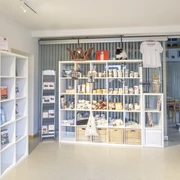 Innenansicht In einem hellen Raum mit modernen, weißen Regalen werden lokale Produkte und Souvenirs stilvoll präsentiert. Ein großes Schiebetor aus Glas im Hintergrund trägt zur offenen und einladenden Atmosphäre bei.