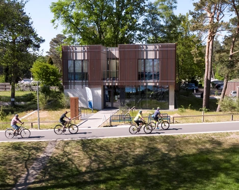 Das Naturpark-Haus mit seiner modernen Glasfassade ist von Radfahrern auf einer Allee umgeben.