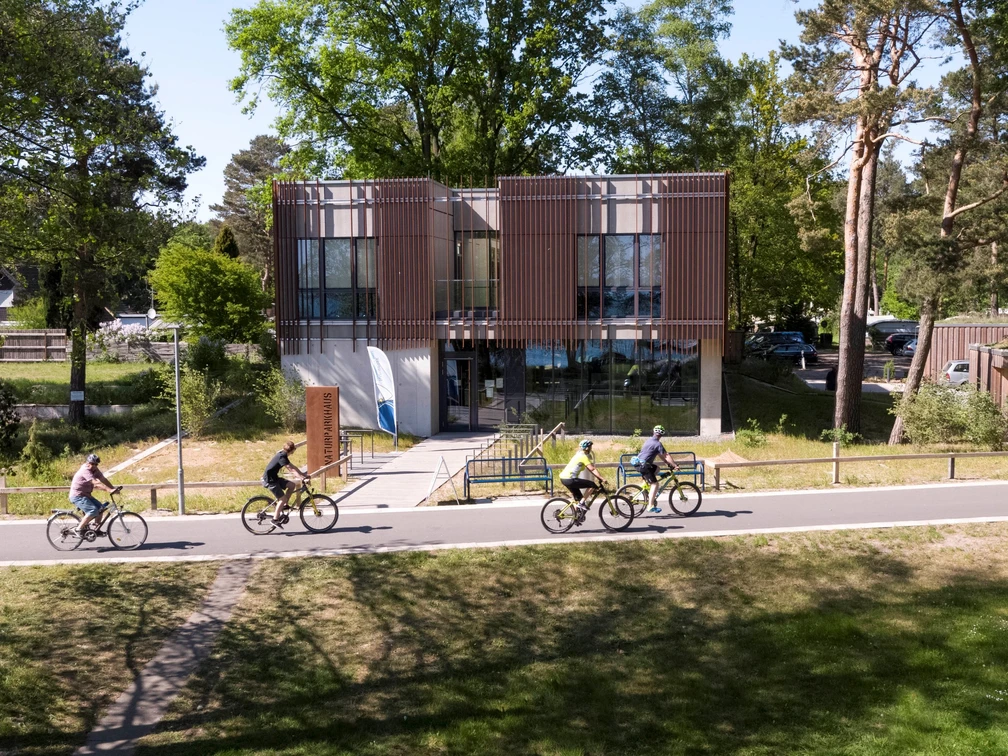 Naturpark-Haus Das Naturpark-Haus mit seiner modernen Glasfassade ist von Radfahrern auf einer Allee umgeben.