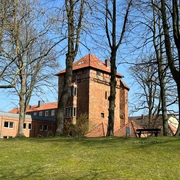 Stockturm Backstein-Turm mit roten Ziegeldächern, umgeben von kahlen Bäumen, vor blauem Himmel im Hintergrund.