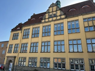 Baugewerkschule Historisches Gebäude mit gelber Fassade, vielen Fenstern und markanter Dachform bei blauem Himmel.