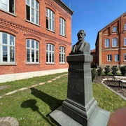 Rhien-Büste Büste des Heinrich Hermann Reineke vor einer roten Backsteinfassade in grünem Außenbereich.