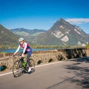 Eine Bikerin auf einem Rennrad unterwegs zwischen Interlaken und Spiez, im Hintergrund der Thunersee sowie der Harder