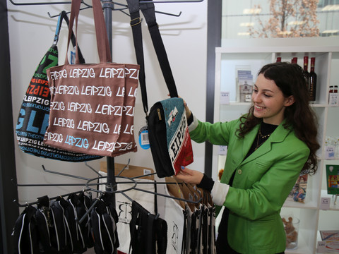 Eine Besucherin der Stadt Leipzig schaut sich in der Tourist-Information Leipzig die Souvenirs und im Speziellem die Taschen an