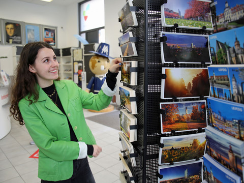Eine Besucherin der Stadt Leipzig schaut sich in der Tourist-Information Leipzig die Postkarten näher an
