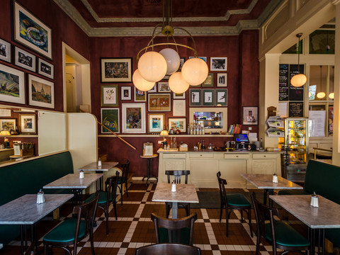 Blick in den histrorischen Gastraum des Café Maître mit den schmiedeeisernen Jugenstilmöbeln und vielen Fotos an den dunkelroten Wänden, Kaffeehaus, Gastronomie, Restaurant