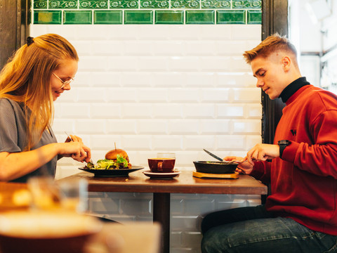 Zwei junge Menschen sitzen vor dem industriellen Interieur der Dankbar und probieren sich durch die Speisekarte, Cafe, Restaurant, gastronomie