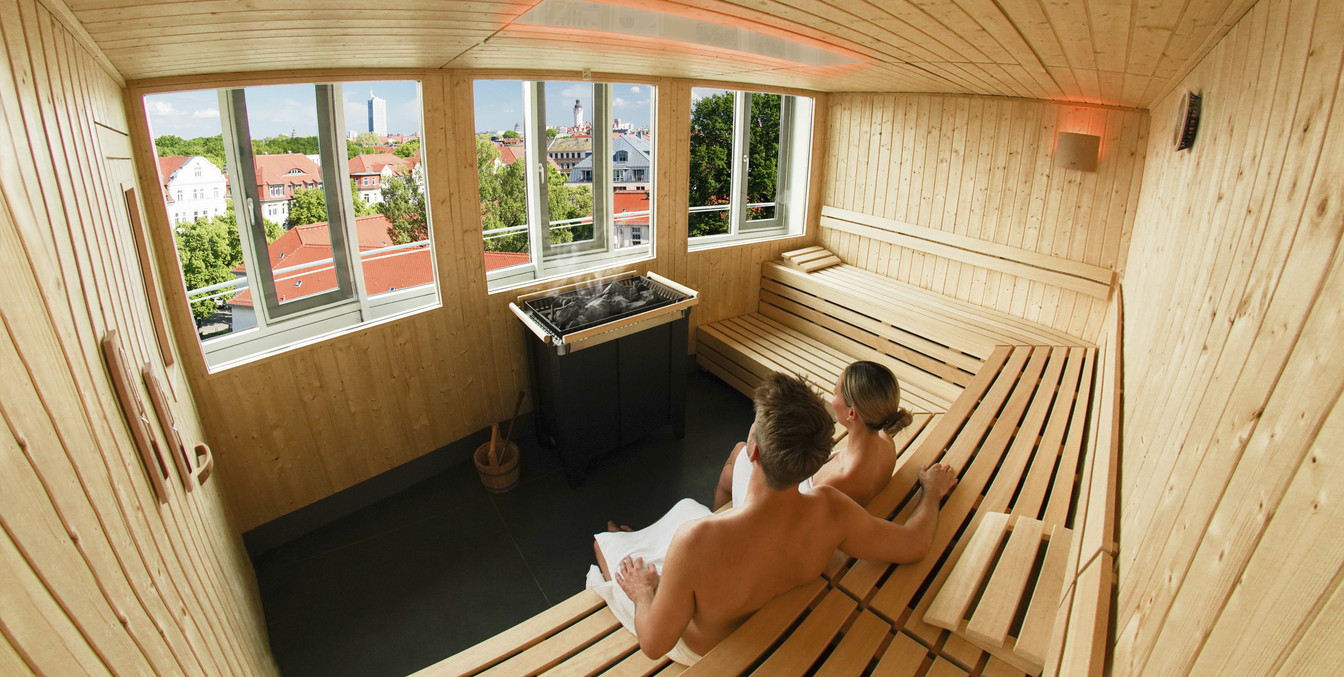 Zwei Personen sitzen in einer Sauna und schauen auf die Leipziger Skyline, Wellness in Leipzig, Sauna