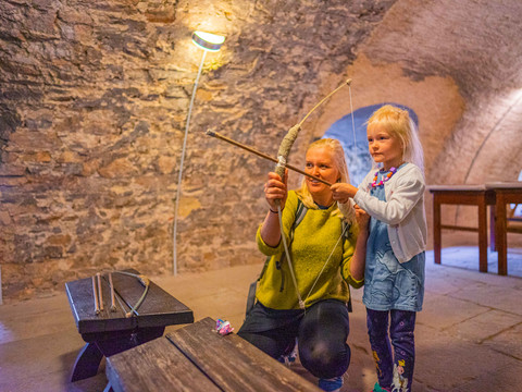 Eine Mutter probiert gemeinsam mit ihrer Tochter Bogenschießen im Schloss Frohburg in der Leipzig Region