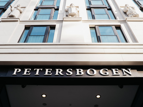 Bild vom Schriftzug "Petersbogen" über dem Eingang zu der Einkaufspassage am Burgplatz in Leipzig, darüber sieht man 3 Sandsteinfiguren von Akteuren der Leipziger Disputation