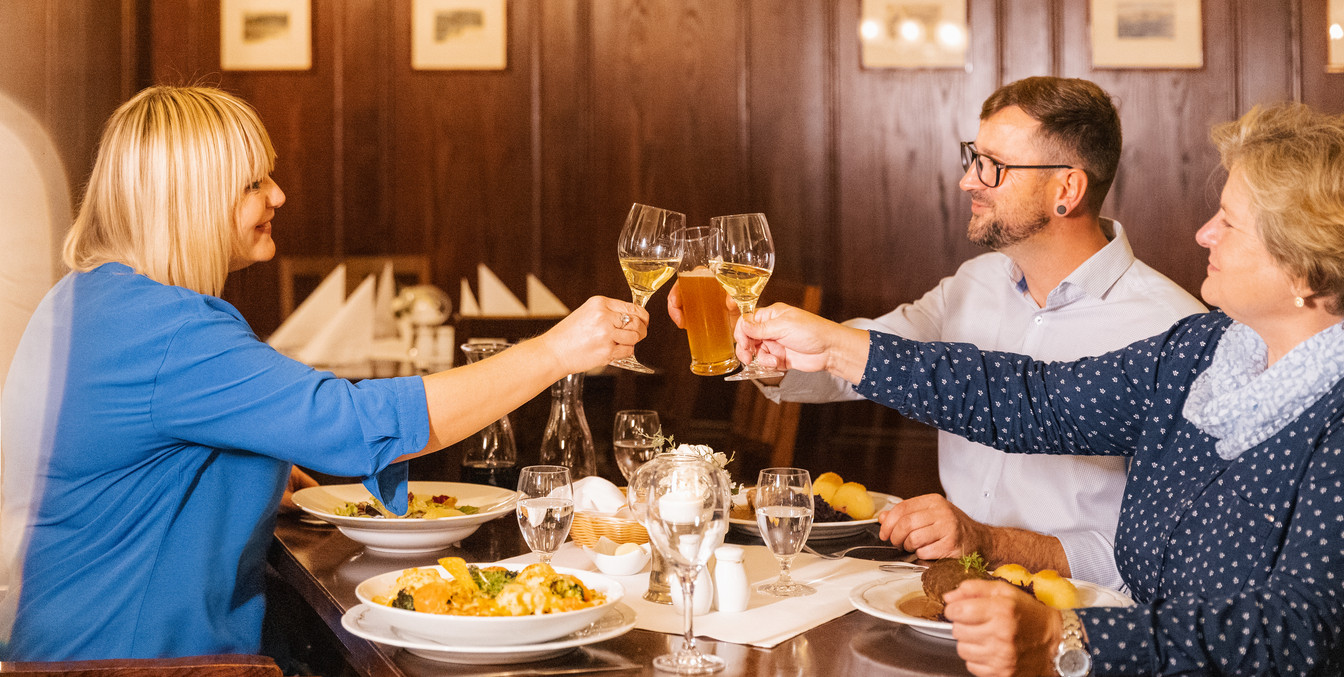 Drei Gäste in Auerbachs Keller stoßen bei gedecktem Tisch mit ihren Wein- oder Biergläsern an