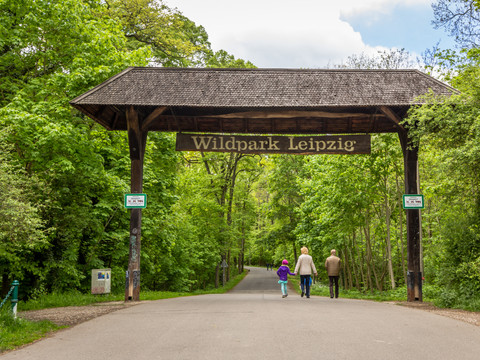 Eingangstor des Wildpark Leipzig, durch das eine Familie geht, Freizeit, Familienurlaub, Tiere, Wald
