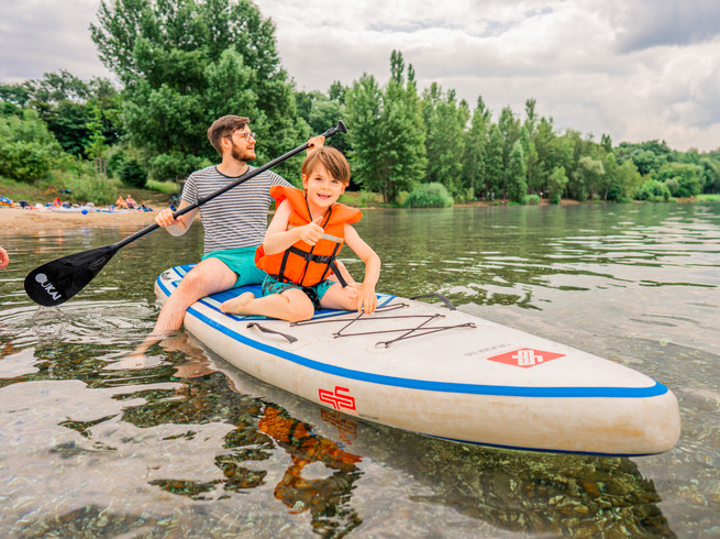 Blick auf ein SUP Paddle mit einem Jungen und seinen Vater, die auf dem Cospudener See im Sommer paddeln, Badesee, Freizeit, Familie