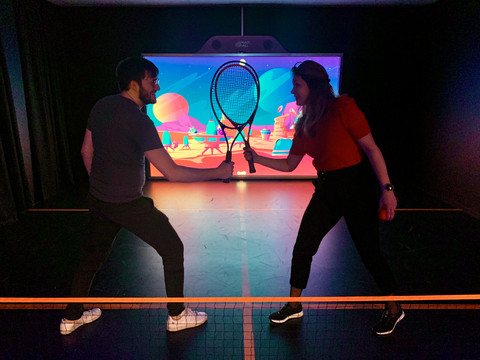 Zwei Personen halten Tennisschläger wie Fechtdegen vor der Leinwand in der Multiplex-Lounge beim Team-Duell in Leipzig, Freizeitaktivitäten in Leipzig