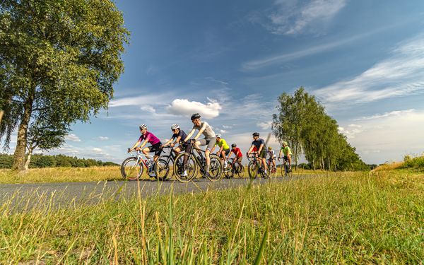 Rennradgruppe untwerwegs durch Wiesen und Wolkenspiel