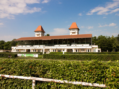 Blick auf das Veranstaltungsgebäude auf der großen Galopprennbahn; weiße Gemäuer mit roten Dächern und Türmchen, Gaststätte, Eventlocation