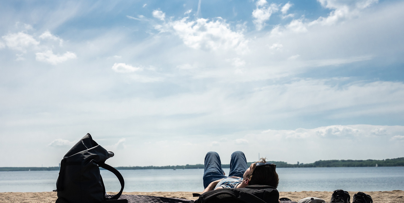 Ein junger Mann liegt am Sandstrand des Cospudener Sees mit Blick auf das Wasser und genießt die Sonne, Freizeit, Wasser, Leipziger Neuseenland