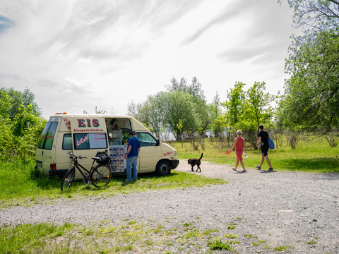 Am sommerlichen Cospudener See steht ein Eiswagen, darum spazierende Menschen mit Hund und Fahrrad, Sommer, Freizeit, Region, Leipziger Neuseenland