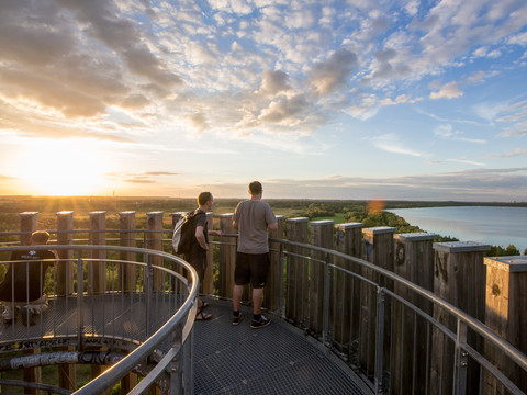 Zwei Männer stehen auf dem Aussichtstum Bistumshöhe und genießen einen Weitblick über den Cospudener See und die angrenzenden Grünflächen, Freizeit, Leipziger Neuseenland