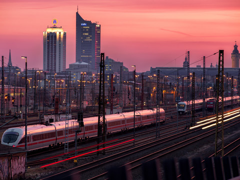 Züge fahren in den Leipziger Hauptbahnhof ein, Im Hintergrund das Krochhochhaus, das Neue Rathaus und das City-Hochhaus im Sonnenuntergang