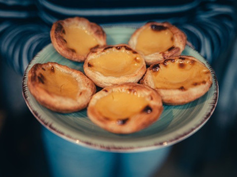Süße Pasteis werden auf einem blauen Teller serviert und von einer Person in der Hand gehalten, Kulinarik, Stadtführung, Cafés, Genuss