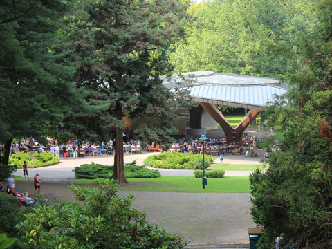 Blick in den grünen Kurpark und auf die Schmetterlingsbühne, vor der viele Menschen bei einer Open Air Veranstaltung sitzen, Freizeit, Kultur, Veranstaltungen